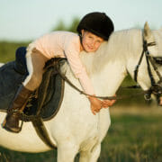 A small child on a grey pony, hugging her beloved pony club mount that is fed a balanced diet
